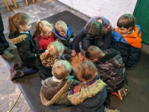 Children surrounding teacher with plastic box filled with sand.